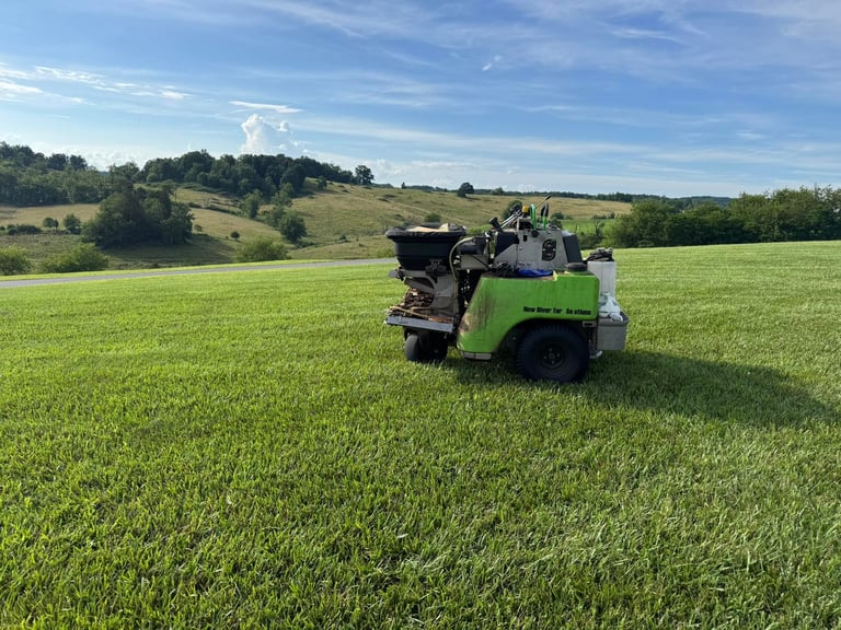 Green agricultural sprayer machine in a large green crop field with rolling hills and trees in the background