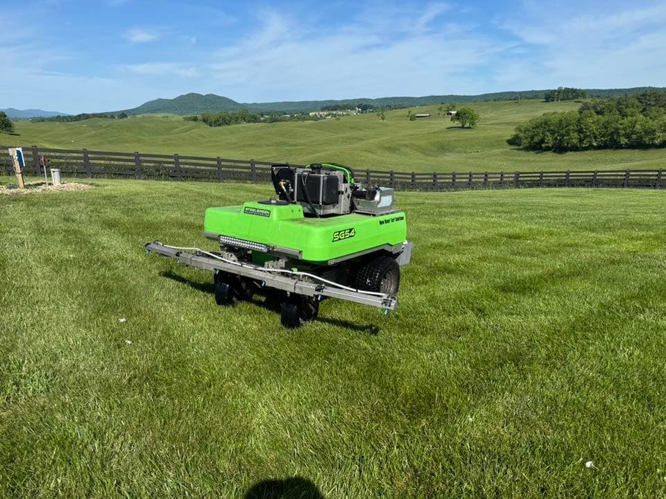 Bright green zero-turn mower with attached trailer on a large green pasture