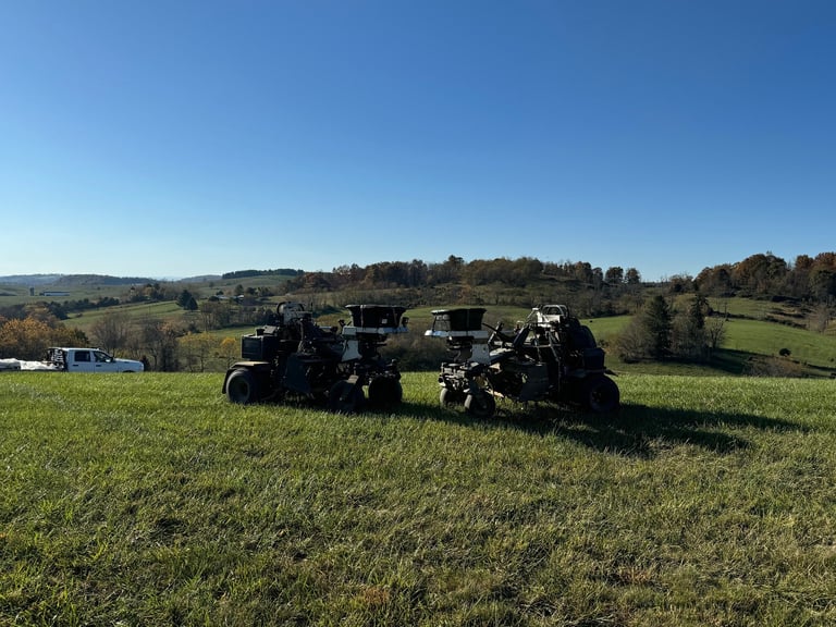 Black tractors parked in a green field with rolling hills and scattered trees under a clear blue sky